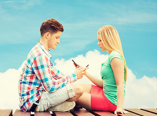 Image showing couple with smartphones sitting on bench over sky
