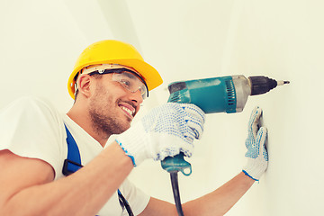 Image showing smiling builder in hardhat drilling wall indoors