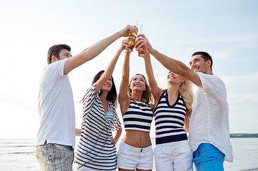 Image showing smiling friends clinking bottles on beach