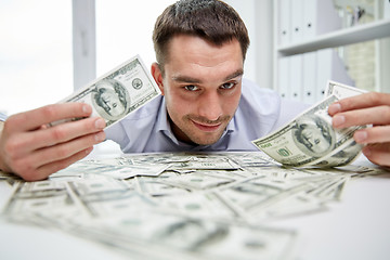 Image showing happy businessman with heap of money in office