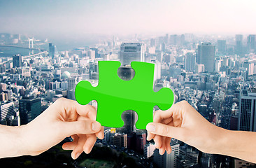 Image showing hands with green puzzle over city background