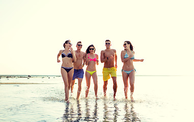 Image showing smiling friends in sunglasses running on beach
