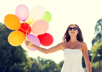 Image showing smiling young woman in sunglasses with balloons