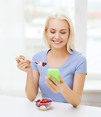 Image showing woman with smartphone eating fruits at home