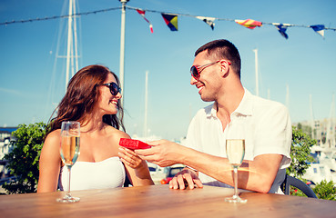 Image showing smiling couple with champagne and gift at cafe