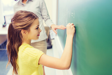 Image showing little smiling schoolgirl writing on chalk board