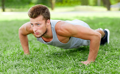 Image showing young man doing push ups on grass in summer park