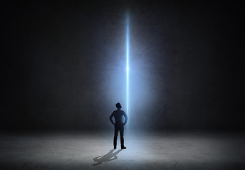 Image showing businessman looking at ray of light over dark room