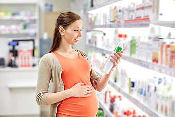 Image showing happy pregnant woman choosing lotion at pharmacy