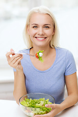 Image showing smiling young woman eating salad at home
