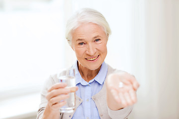 Image showing happy senior woman with water and medicine at home