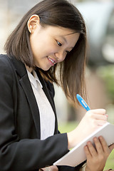 Image showing Young Asian female business executive writing on notepad