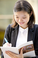 Image showing Young Asian female business executive writing on notepad