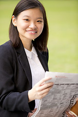 Image showing Young Asian female business executive reading newspaper