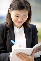 Image showing Young Asian female business executive writing on notepad