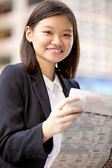 Image showing Young Asian female business executive reading newspaper