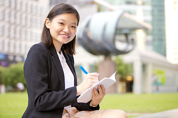 Image showing Young Asian female business executive writing on notepad