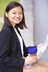 Image showing Young Asian female business executive reading newspaper