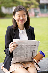 Image showing Young Asian female business executive reading newspaper