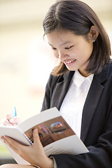 Image showing Young Asian female business executive writing on notepad