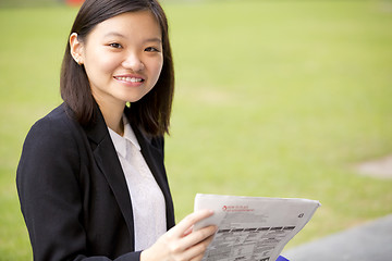 Image showing Young Asian female business executive reading newspaper