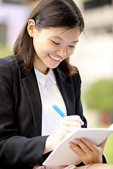 Image showing Young Asian female business executive writing on notepad