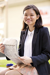 Image showing Young Asian female business executive reading newspaper