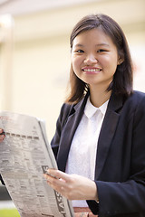 Image showing Young Asian female business executive reading newspaper