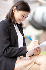 Image showing Young Asian female business executive writing on notepad