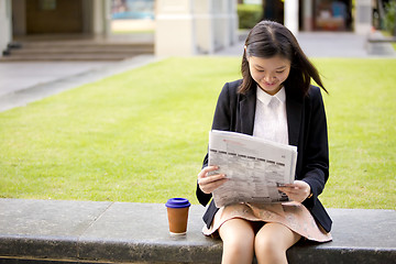 Image showing Young Asian female business executive reading newspaper