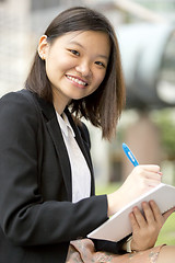 Image showing Young Asian female business executive writing on notepad