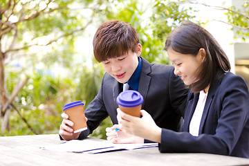 Image showing Young Asian female and male business executive reading newspaper