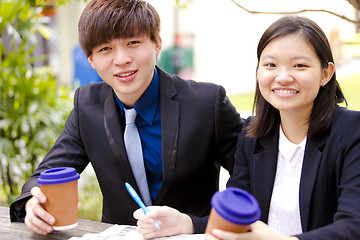 Image showing Young Asian female and male business executive reading newspaper