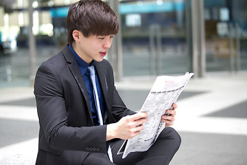 Image showing Young Asian male business executive reading newspaper