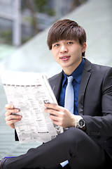 Image showing Young Asian male business executive reading newspaper