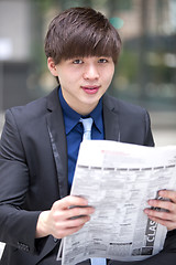 Image showing Young Asian male business executive reading newspaper