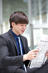 Image showing Young Asian male business executive reading newspaper