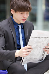 Image showing Young Asian male business executive reading newspaper