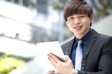 Image showing Young Asian business executive in suit holding tablet and coffee