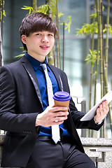 Image showing Young Asian business executive in suit holding tablet and coffee