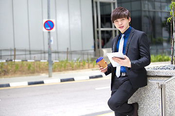 Image showing Young Asian business executive in suit holding tablet and coffee