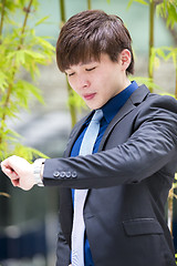 Image showing Young Asian business executive in suit looking at time