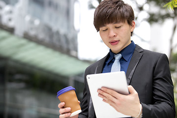 Image showing Young Asian business executive in suit holding tablet and coffee