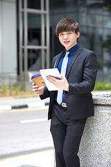Image showing Young Asian business executive in suit holding tablet and coffee