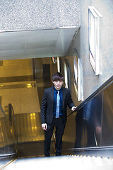 Image showing Young Asian business executive in suit going up escalator