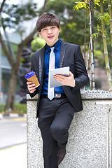 Image showing Young Asian business executive in suit holding tablet and coffee