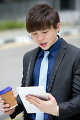 Image showing Young Asian business executive in suit holding tablet and coffee