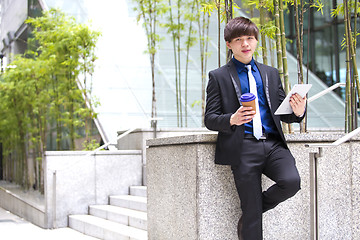 Image showing Young Asian business executive in suit holding tablet and coffee