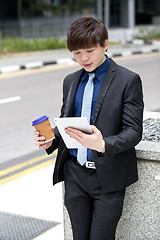 Image showing Young Asian business executive in suit holding tablet and coffee