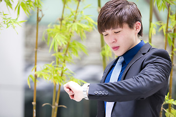 Image showing Young Asian business executive in suit looking at time